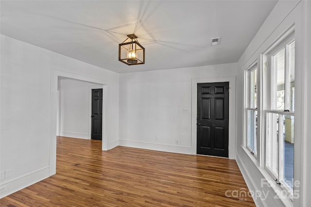 empty room with wood finished floors, visible vents, and baseboards