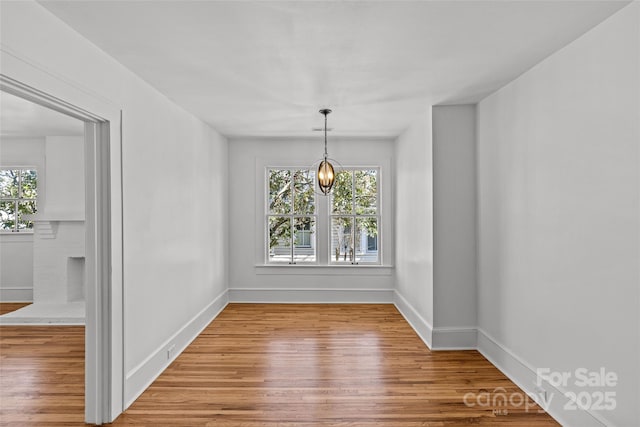 unfurnished dining area with plenty of natural light, an inviting chandelier, and wood finished floors