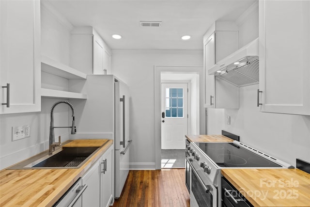 kitchen with visible vents, butcher block countertops, stainless steel range with electric stovetop, exhaust hood, and a sink