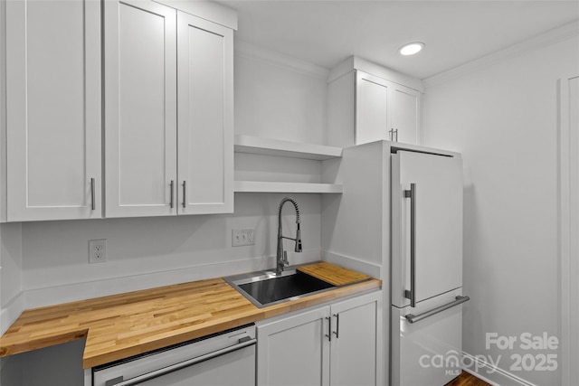 kitchen with a sink, open shelves, white cabinets, butcher block counters, and dishwashing machine