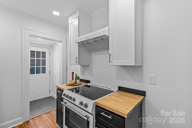 kitchen featuring range hood, light wood-style flooring, butcher block counters, stainless steel electric range oven, and ornamental molding
