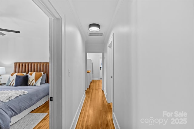 hallway with baseboards, light wood-type flooring, crown molding, and visible vents