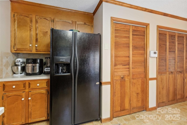 kitchen featuring brown cabinetry, black fridge, light countertops, and ornamental molding