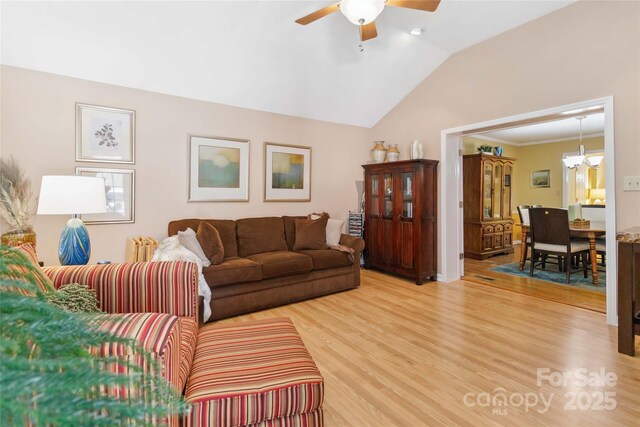 living room with light wood finished floors, ceiling fan with notable chandelier, and lofted ceiling