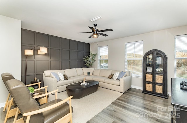 living room with a ceiling fan, baseboards, visible vents, a decorative wall, and light wood-type flooring