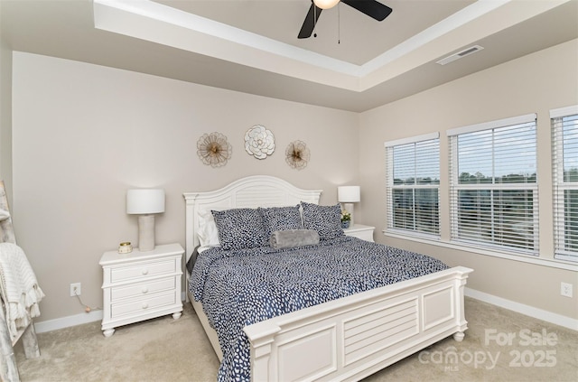 bedroom featuring a tray ceiling, light colored carpet, visible vents, and baseboards