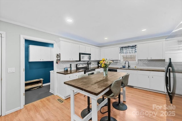 kitchen with a sink, stainless steel appliances, light wood-style floors, and white cabinets
