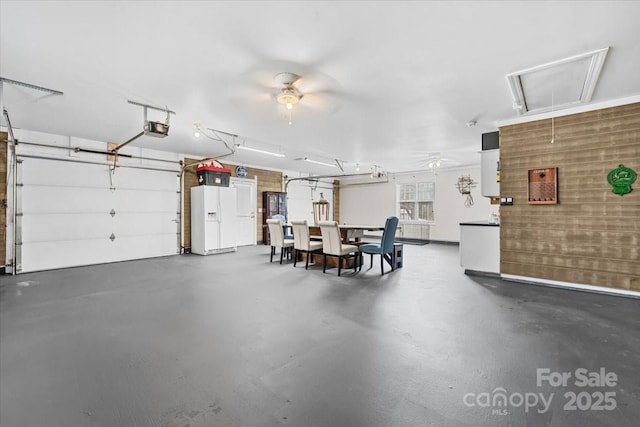 garage featuring ceiling fan, white fridge with ice dispenser, and a garage door opener