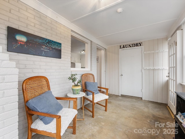 living area featuring unfinished concrete floors, brick wall, and ornamental molding