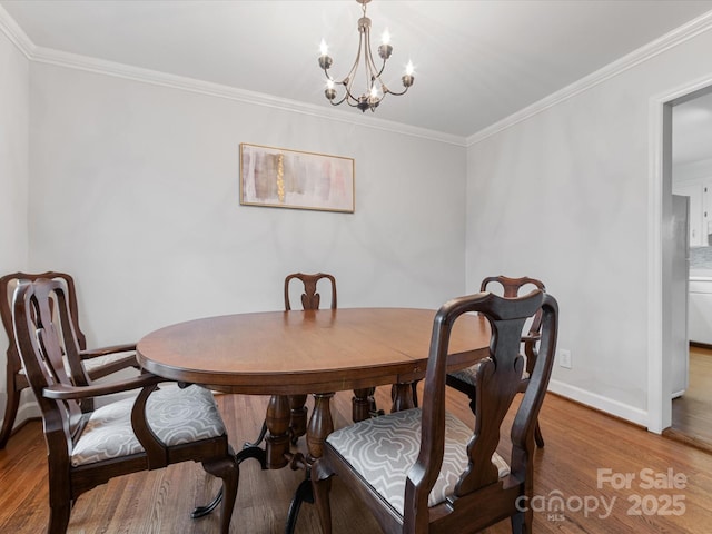 dining area with an inviting chandelier, crown molding, light wood-style floors, and baseboards