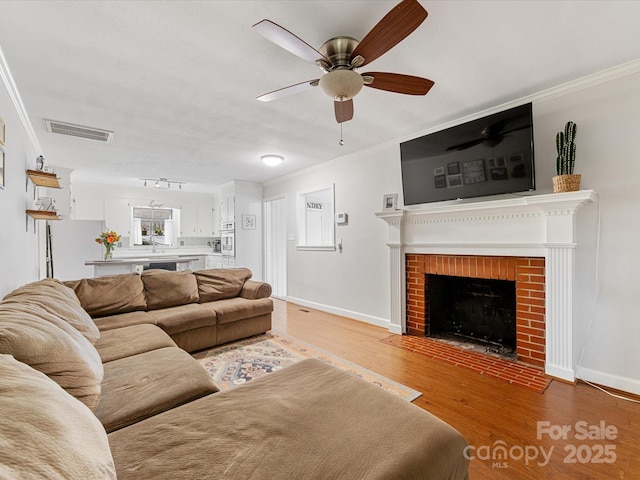 living area featuring visible vents, ornamental molding, wood finished floors, baseboards, and a brick fireplace