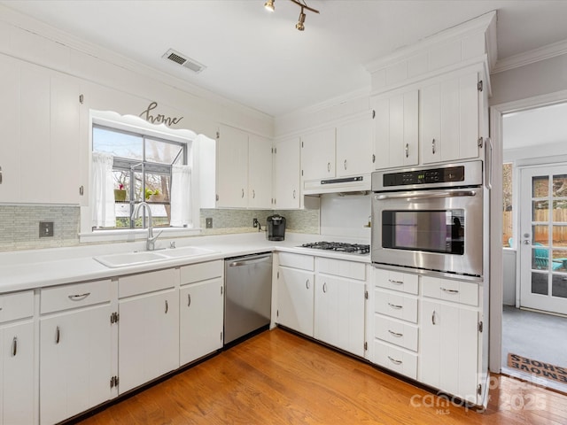 kitchen with visible vents, a sink, under cabinet range hood, appliances with stainless steel finishes, and crown molding