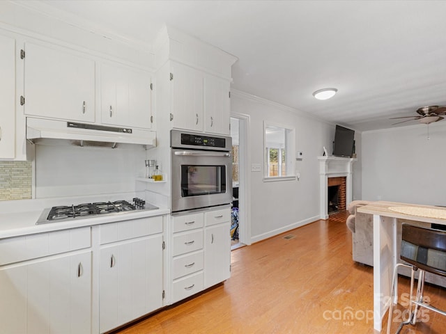 kitchen with light wood-style flooring, under cabinet range hood, white cabinetry, appliances with stainless steel finishes, and light countertops