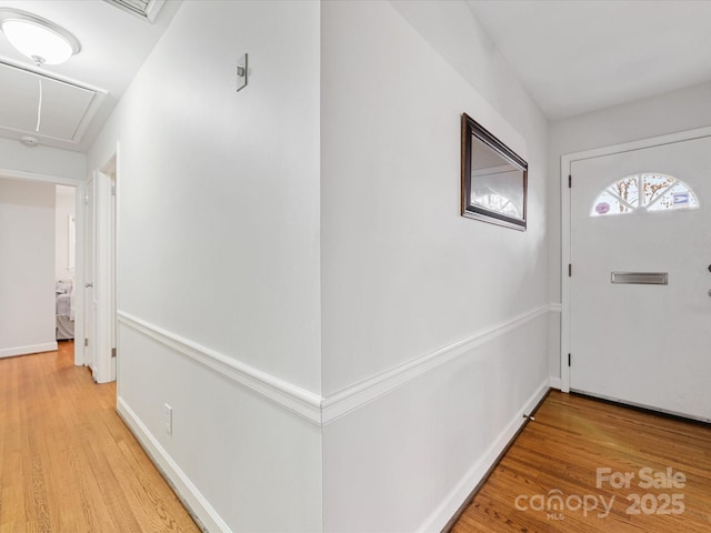 hall with baseboards, attic access, and light wood-style floors