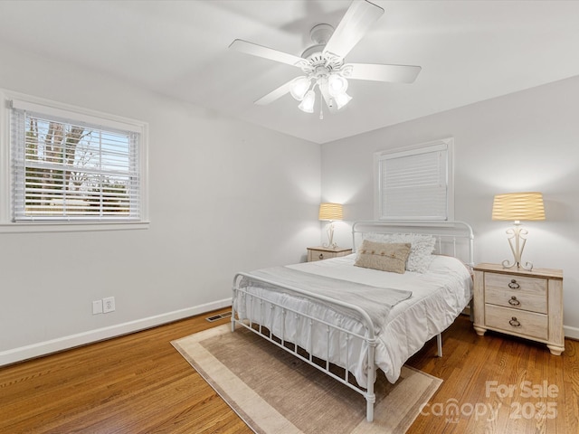 bedroom with visible vents, baseboards, wood finished floors, and a ceiling fan