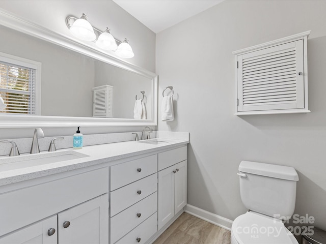 bathroom with a sink, baseboards, toilet, and double vanity