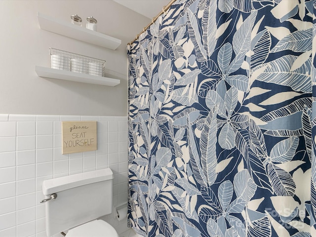 bathroom featuring a wainscoted wall, curtained shower, toilet, and tile walls