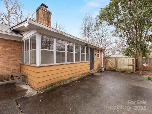 view of side of property with a sunroom, brick siding, a chimney, and fence