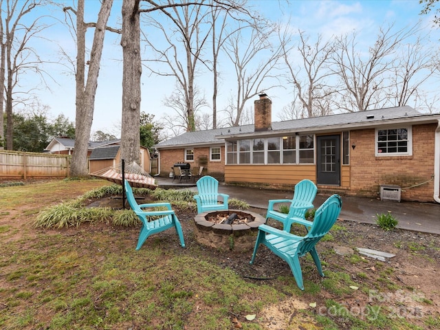 back of house featuring fence, an outdoor fire pit, a sunroom, a chimney, and brick siding