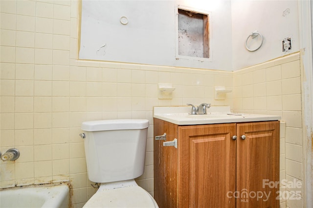 full bath featuring vanity, tile walls, toilet, and wainscoting