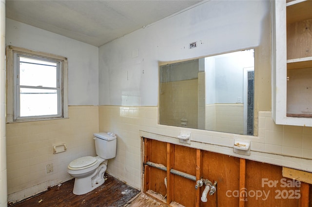 bathroom featuring tile walls, toilet, wood finished floors, and wainscoting