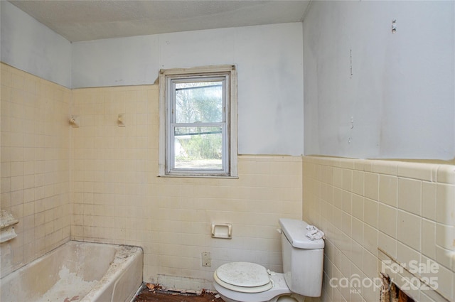 bathroom with tile walls, toilet, a bathing tub, and wainscoting