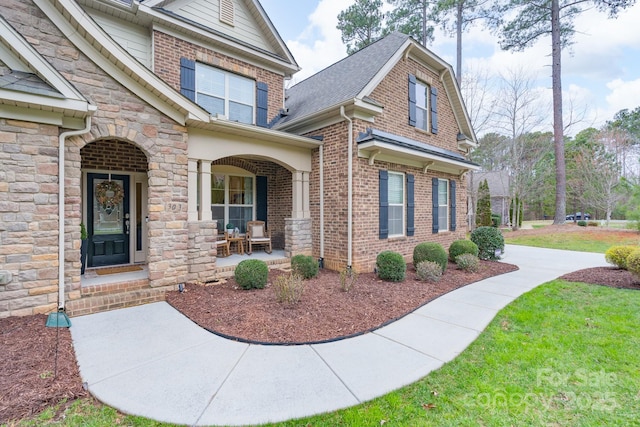 entrance to property with a yard, stone siding, brick siding, and a porch