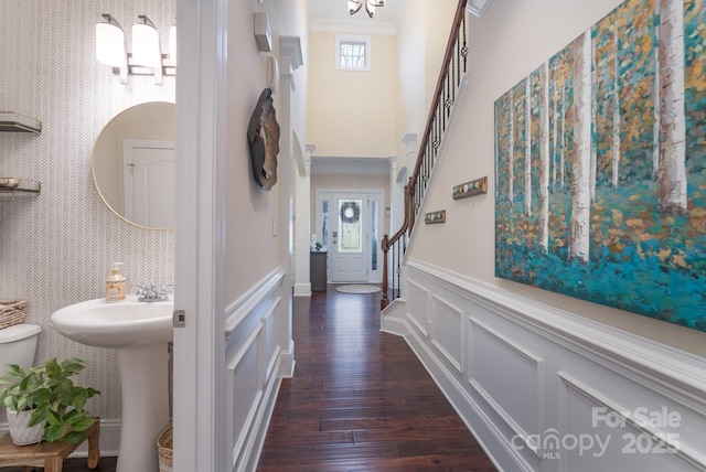 corridor featuring a wainscoted wall, dark wood-style floors, stairway, crown molding, and a decorative wall