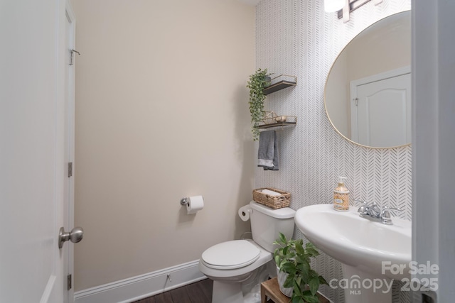 bathroom featuring toilet, wood finished floors, baseboards, and a sink