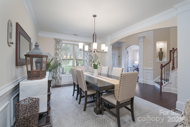 dining space featuring wood finished floors, a decorative wall, arched walkways, wainscoting, and crown molding