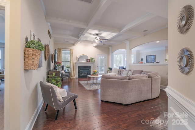 living room with baseboards, coffered ceiling, dark wood finished floors, a glass covered fireplace, and beamed ceiling