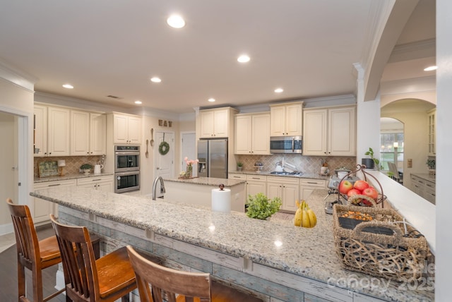 kitchen featuring light stone countertops, a peninsula, stainless steel appliances, a kitchen bar, and crown molding