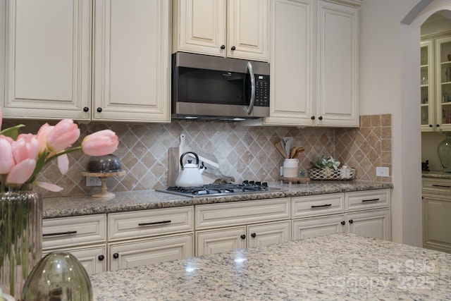 kitchen with decorative backsplash, light stone countertops, arched walkways, and appliances with stainless steel finishes