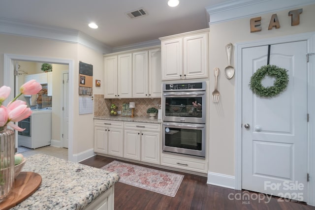 kitchen with visible vents, washer / dryer, ornamental molding, dark wood-type flooring, and double oven