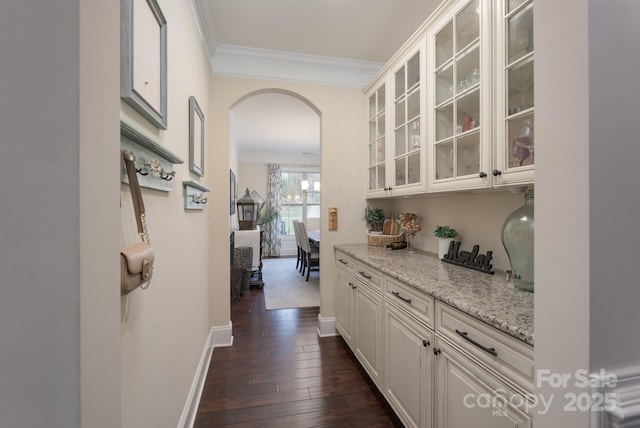 hall with baseboards, arched walkways, ornamental molding, and dark wood-style flooring