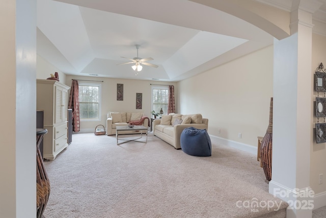 living room with a ceiling fan, a tray ceiling, carpet, and baseboards