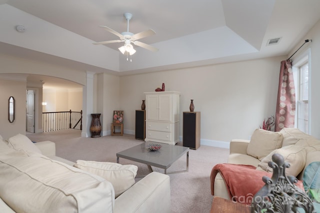 living area featuring visible vents, a tray ceiling, arched walkways, baseboards, and light colored carpet