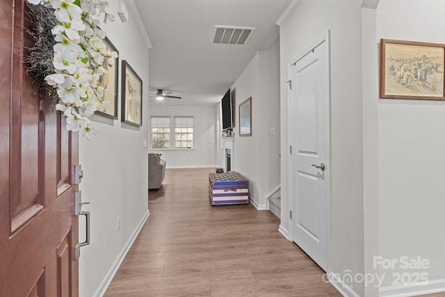 hallway with visible vents, baseboards, wood finished floors, and crown molding