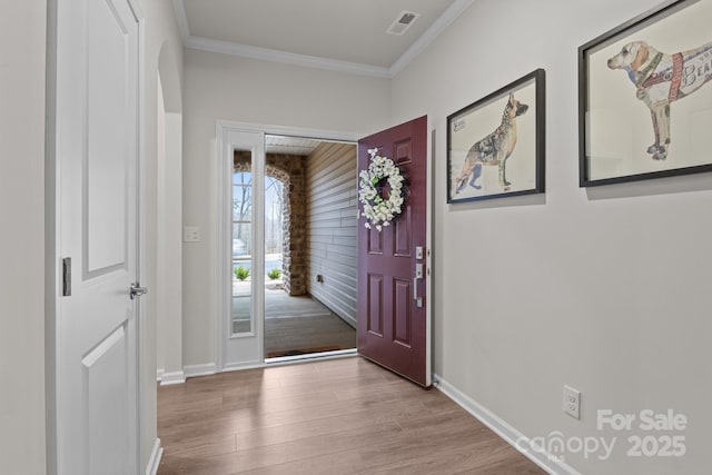 entrance foyer with baseboards, wood finished floors, visible vents, and ornamental molding