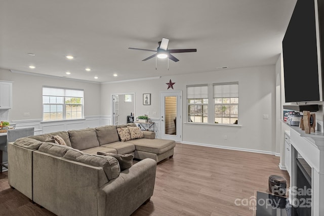 living room featuring a wainscoted wall, light wood-style flooring, recessed lighting, a fireplace, and ceiling fan