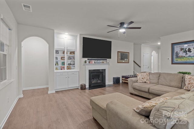 living room with visible vents, a fireplace with flush hearth, light wood-type flooring, arched walkways, and a ceiling fan