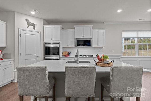 kitchen with visible vents, a kitchen island with sink, light countertops, appliances with stainless steel finishes, and white cabinetry