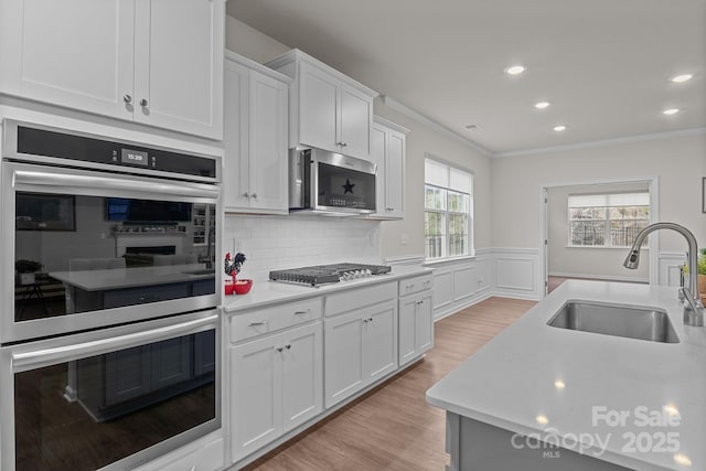 kitchen featuring a wainscoted wall, light countertops, appliances with stainless steel finishes, light wood-style floors, and a sink