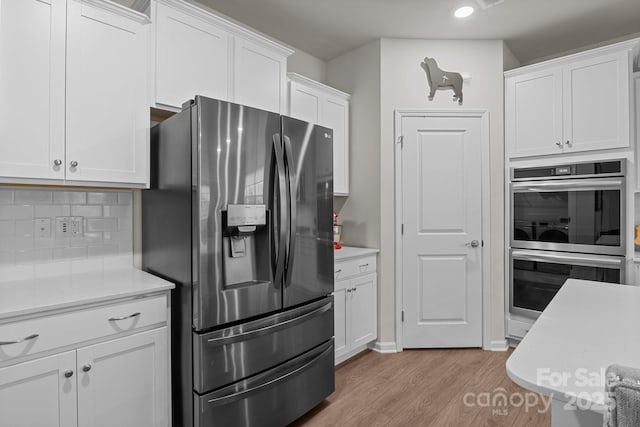 kitchen with light wood finished floors, light countertops, white cabinets, appliances with stainless steel finishes, and backsplash