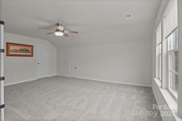 empty room with visible vents, light colored carpet, baseboards, and vaulted ceiling