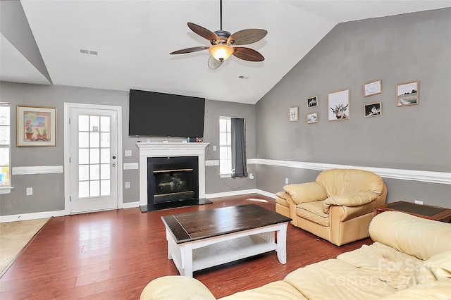 living area featuring visible vents, dark wood-style flooring, ceiling fan, vaulted ceiling, and a glass covered fireplace