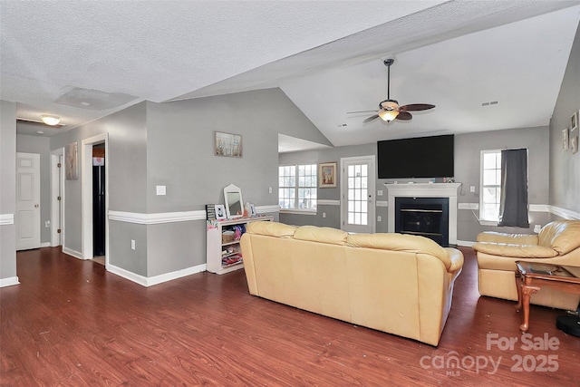 living room with a textured ceiling, a glass covered fireplace, lofted ceiling, ceiling fan, and dark wood-style flooring