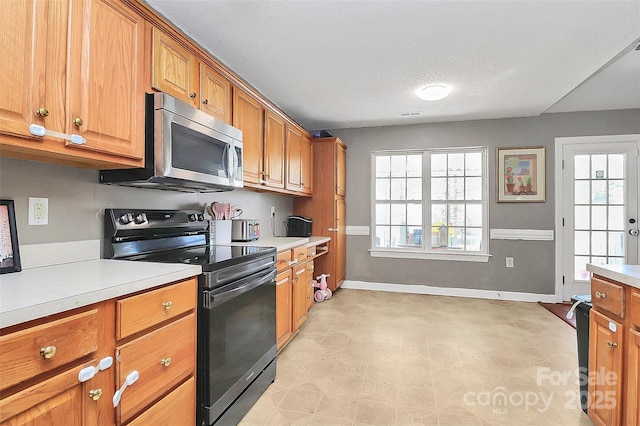 kitchen featuring stainless steel microwave, black range with electric cooktop, brown cabinetry, and light countertops