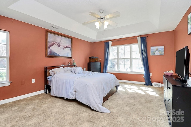 bedroom with a tray ceiling, multiple windows, and baseboards