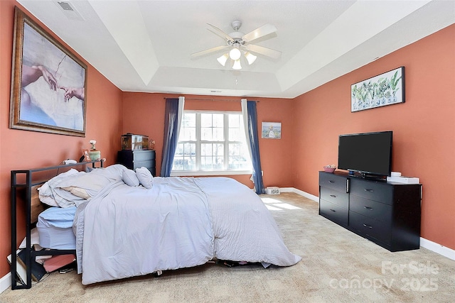 bedroom featuring a ceiling fan, visible vents, baseboards, a tray ceiling, and light colored carpet